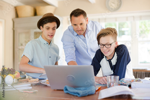 Teenage boys with father using laptop in dining room