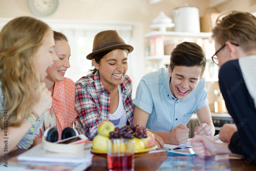 Group of teenagers using together digital tablet at table in kitchen Group of teenagers using together digital tablet at table in kitchen