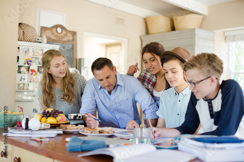 Teenagers with mid adult man sitting at table in dining room