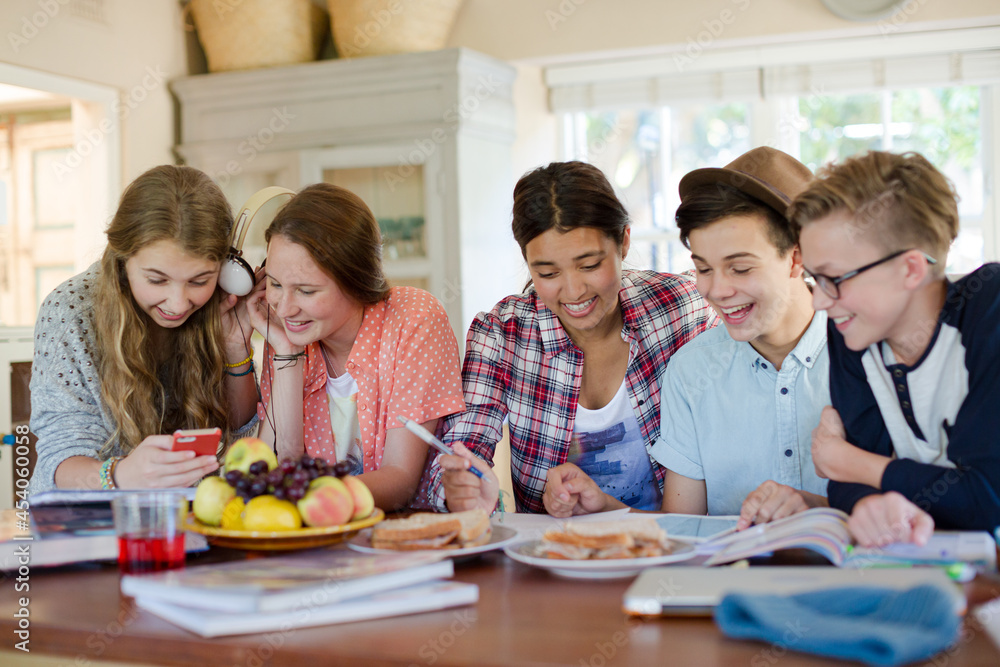 Group of smiling teenagers gathered around table in dining room Group of smiling teenagers gathered around table in dining room