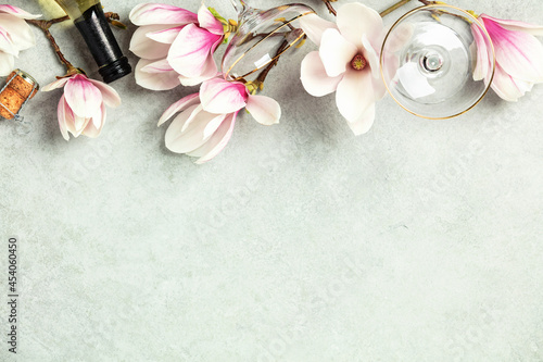 Beautiful flat lay with spring magnolia flowers, wine and glasses on grey stone background