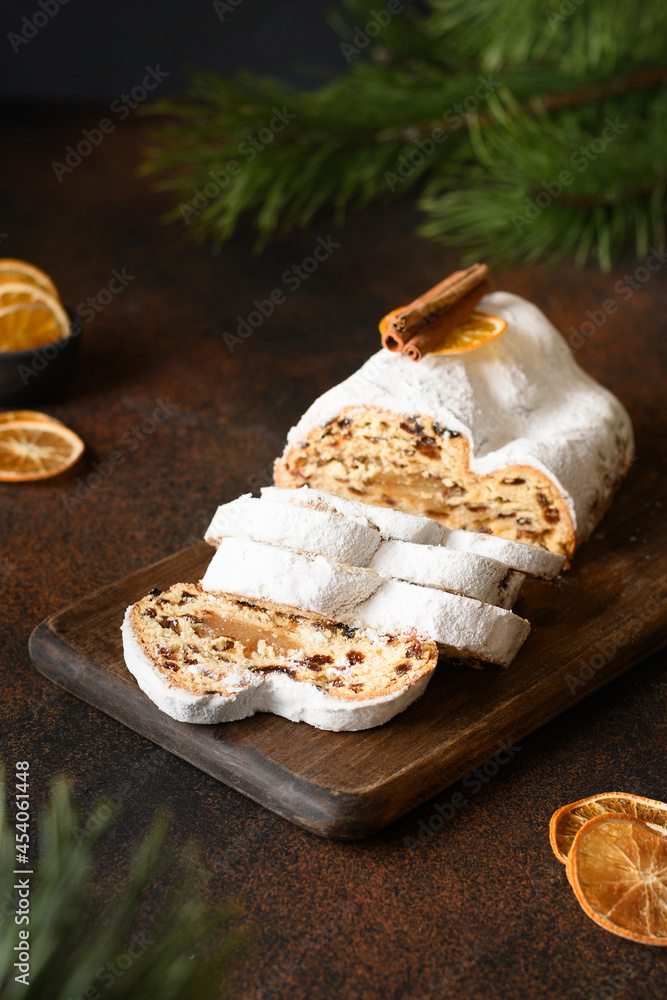 Traditional stollen decorated orange slices on a brown background with evergreen branches. Christmas holiday traditional food. Close up.