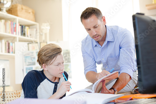 Father helping teenage son doing his homework in room