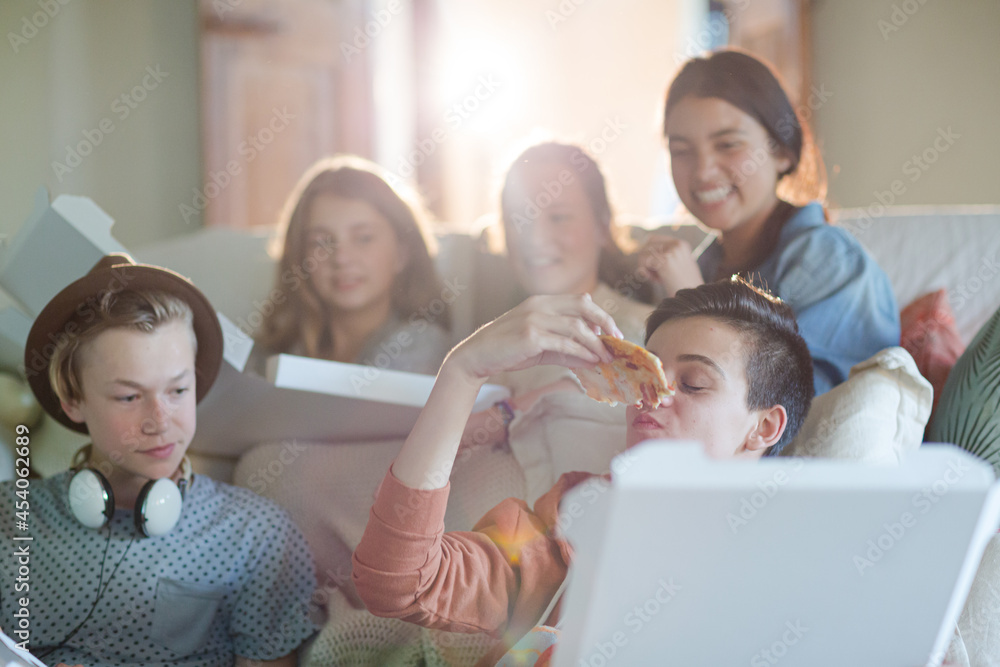 Group of teenagers eating pizza on sofa in living room
