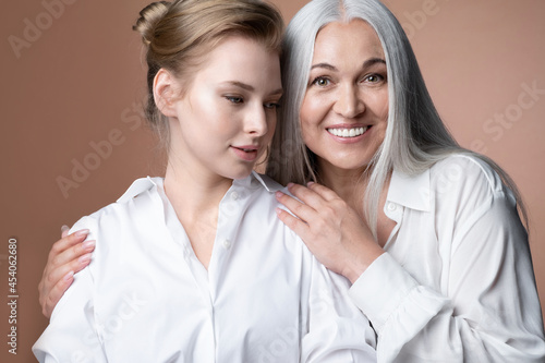Portrait happy smiling mature mother and adult young daughter bonding, embracing shoulders, enjoying free time together, two female generations relations. Natural woman beauty.