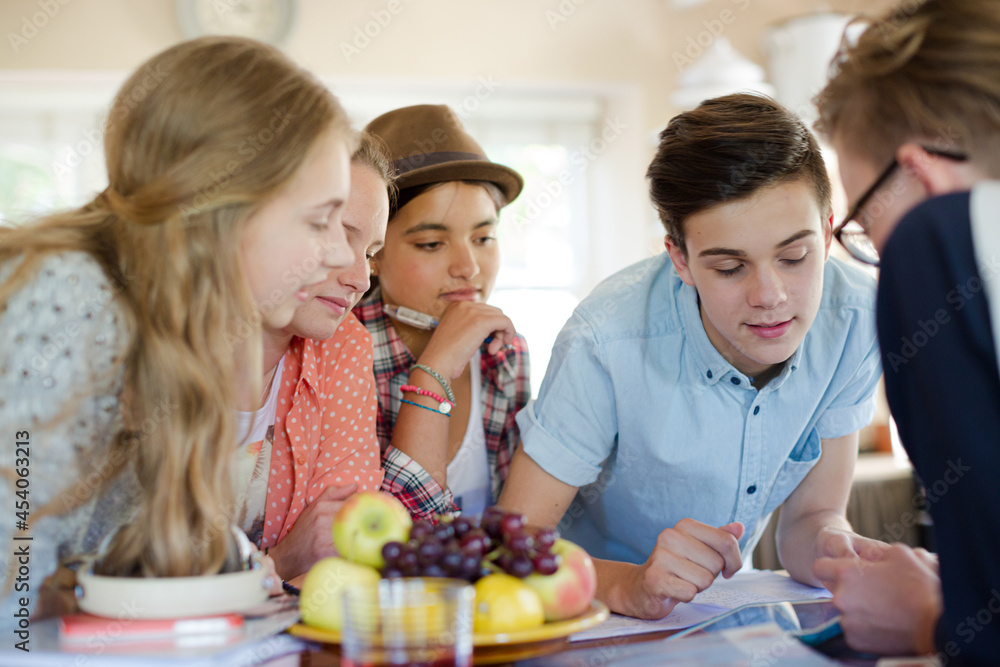 Group of teenagers using together digital tablet at table in kitchen Group of teenagers using together digital tablet at table in kitchen
