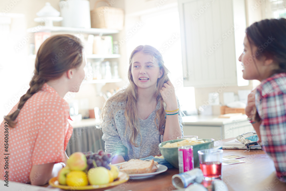 Teenage girls learning at table in kitchen