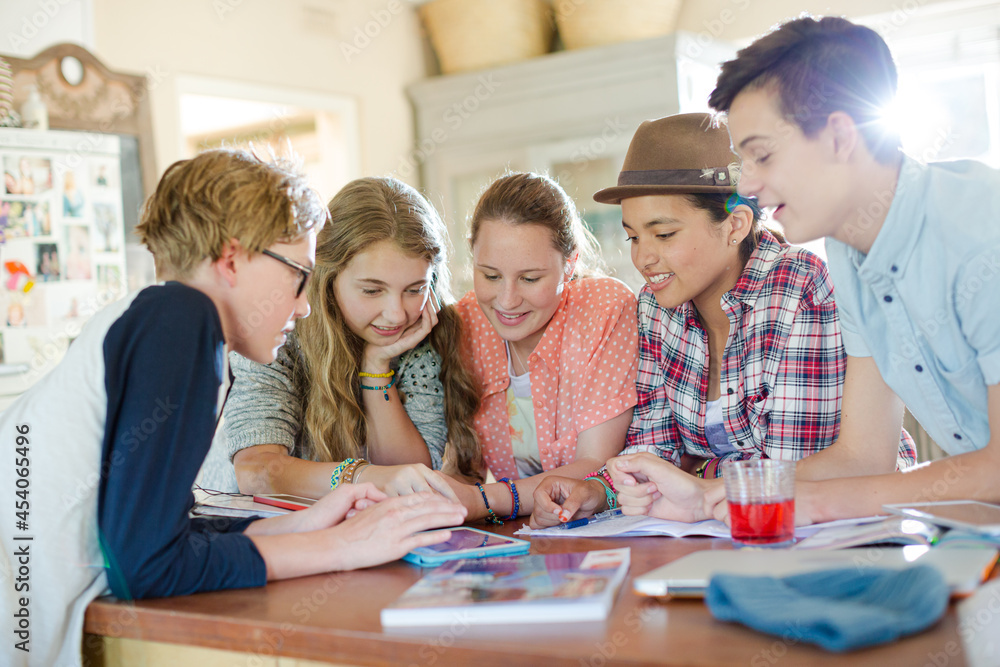 Group of teenagers using together digital tablet at table in kitchen Group of teenagers using together digital tablet at table in kitchen