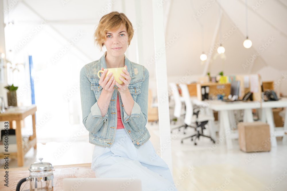 Obraz premium Portrait of woman sitting at desk with laptop and cup in office