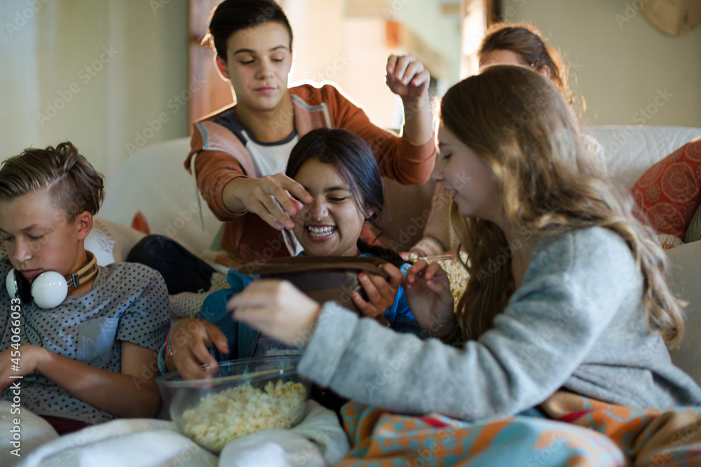 Group of teenagers throwing popcorn on themselves while sitting on sofa