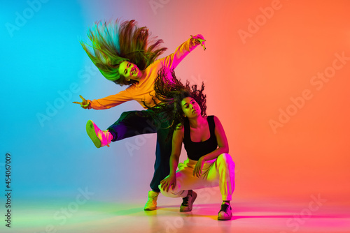 Two beautiful hip-hop girls dancing on gradient blue orange backlground in neon photo
