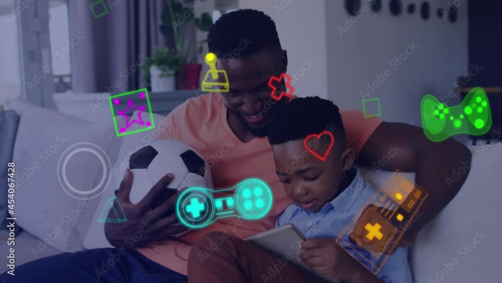 Animation of game media icons over smiling father and son using tablet on couch at home Animation of game media icons over smiling father and son using tablet on couch at home