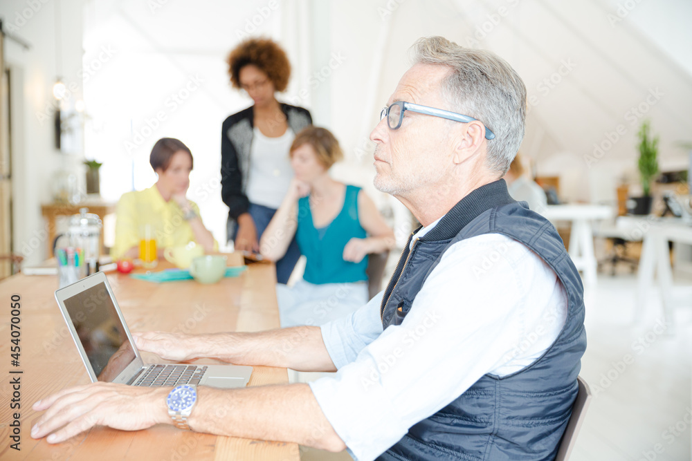 Portrait of man using laptop , woman laughing in background Portrait of man using laptop , woman laughing in background