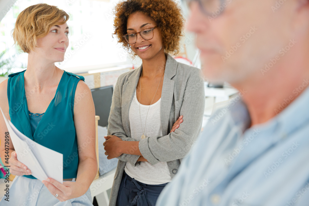 Fototapeta premium Colleagues talking and smiling in office, holding documents