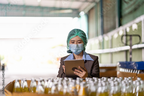 Foto Asian female specialist worker wearing hairnet and protective mask working and checking goods or product of Basil seed with fruit on shelf pallet at beverage factory