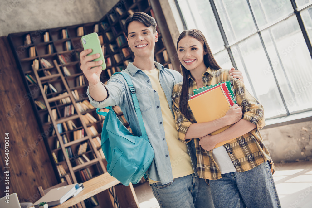 Obraz premium Portrait of two attractive cheerful friends friendship learners hugging taking selfie back to school at loft industrial interior indoors