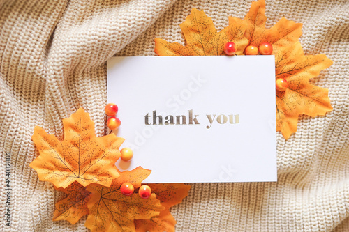 Thank you card on beige knit with yellow maple leaves and autumn berries. Fall theme composition in natural light. Thanksgiving holiday. Special thank you note.	