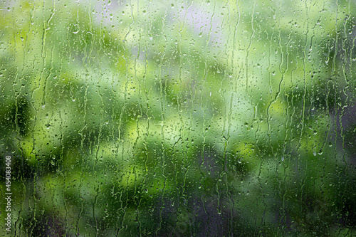 Close up on raindrop on glass with blurry background of tree.