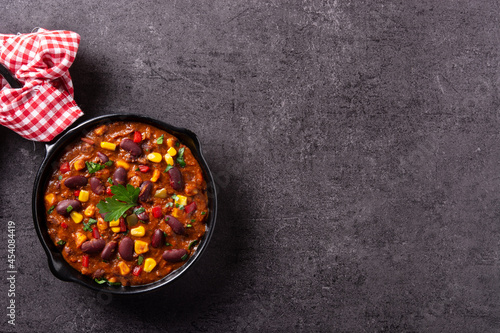 Traditional mexican tex mex chili con carne in iron pan on black background. Top view. Copy space
