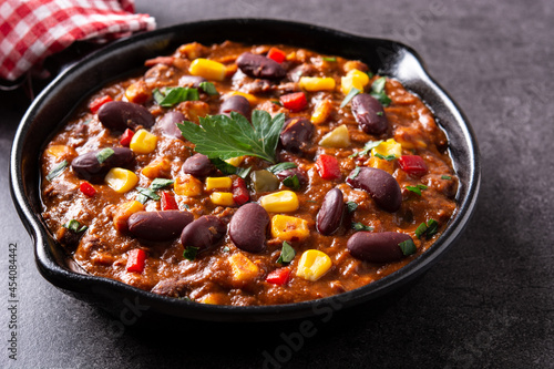 Traditional mexican tex mex chili con carne in iron pan on black background