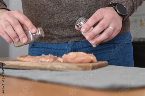 man with watch cutting a chicken breast on a board at the kitchen table