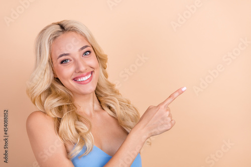 Photo of cute adorable young lady wear blue singlet smiling pointing finger empty space isolated beige color background