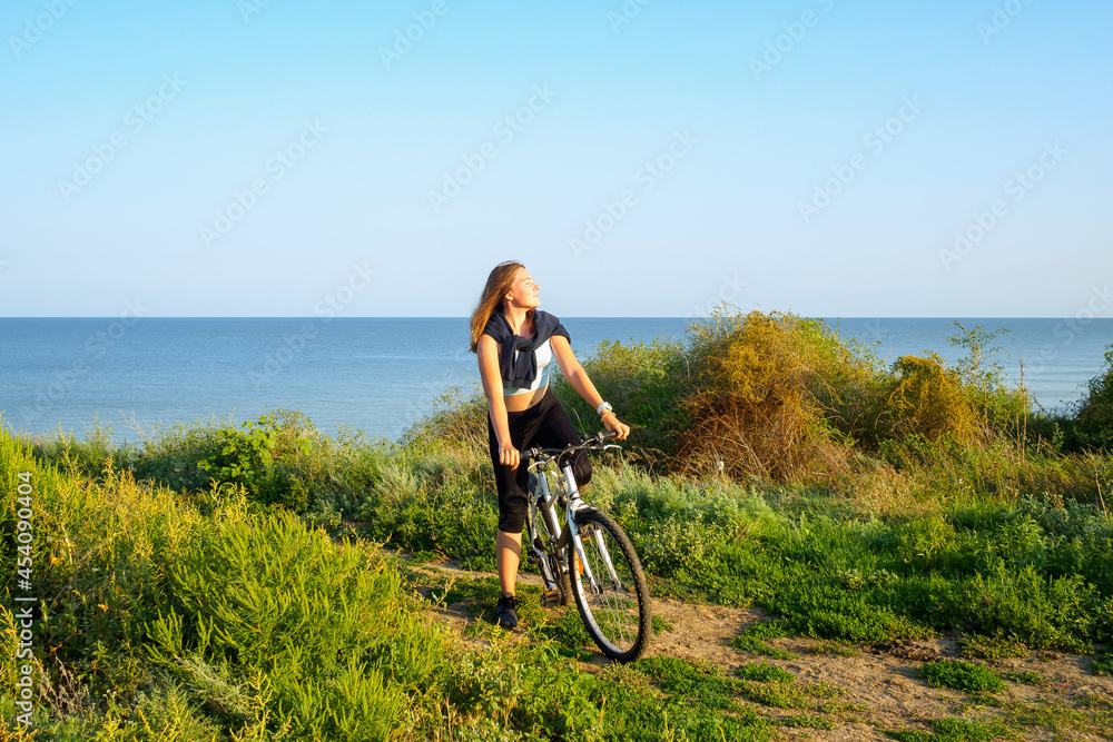 Sportive attractive young girl with a white mountain bike outdoors on a cliff near the sea. Sports training on a summer morning at sunrise. Sportive attractive young girl with a white mountain bike outdoors on a cliff near the sea. Sports training on a summer morning at sunrise.