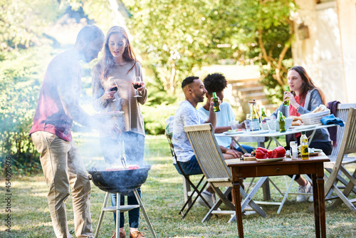 Young man preparing food in barbecue by his friends sitting at table photo