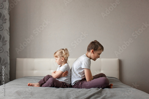 brother and sister have quarreled and sitting with their backs to each other home on bed. concept childhood, family