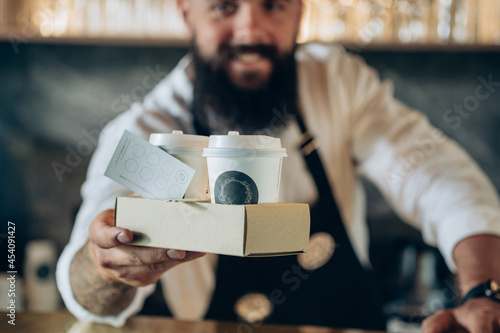 An Anonymous Barista Serving Two Take Away Paper Cup with Espresso to You.

Smiling waiter giving disposable tray with two cups of take out coffee with loyalty card in a coffee shop, focus on hands.