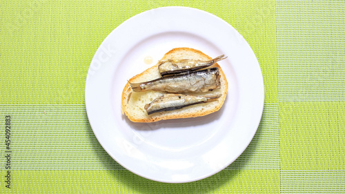 Fish sprats on a piece of white bread on a plate.