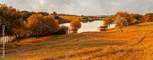 Beautiful rural landscape with meadow and lake. Tranquil autumn evening view over fields with pond in foreground.