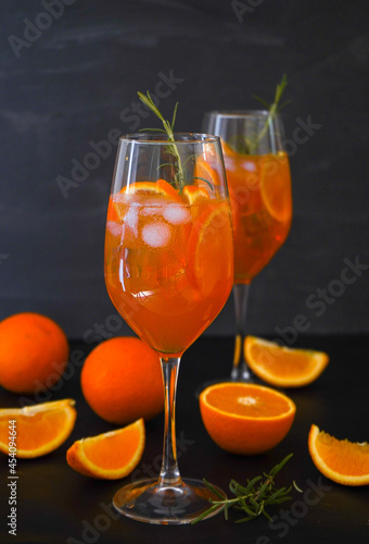 Aperol spritz is a summer drink served in a glass with aperol, prosecco, soda and orange slice. Glasses of icy cocktail in a wine glass and a rosemary at the bar. Black background. Refreshing concept.