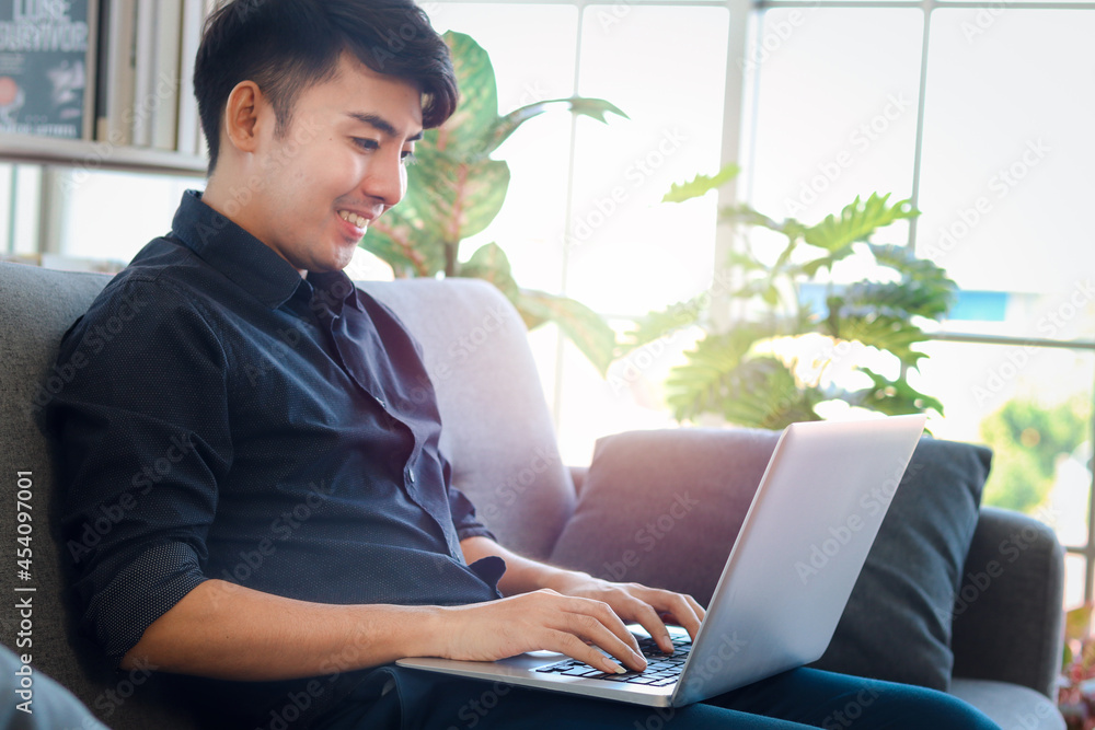 Asian young businessman typing on keyboard laptop computer while sitting on sofa couch in his apartment, freelancer working online in living room Asian young businessman typing on keyboard laptop computer while sitting on sofa couch in his apartment, freelancer working online in living room