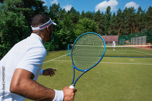 African american sportsman playing tennis with blurred friend on court © LIGHTFIELD STUDIOS