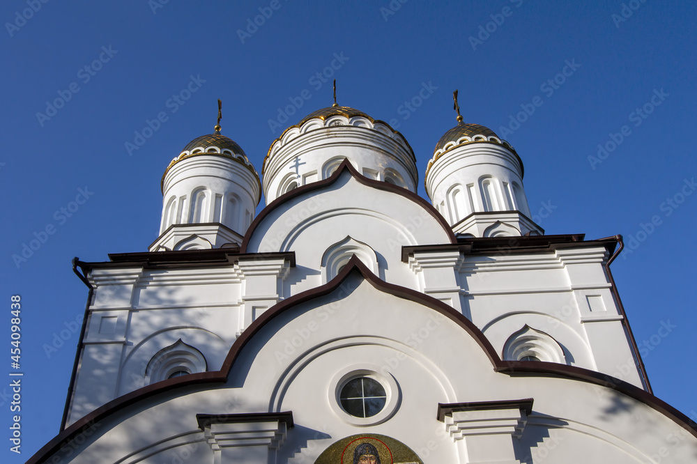 Fototapeta premium Gilded domes and white walls of a Christian church against a cloudless sky