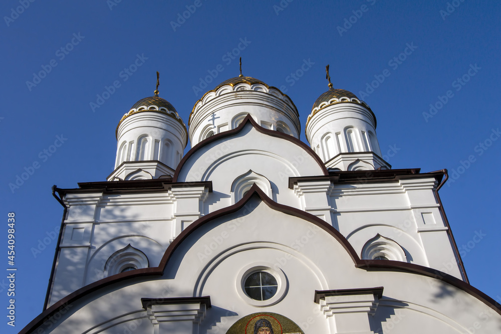 Gilded domes and white walls of a Christian church against a cloudless sky