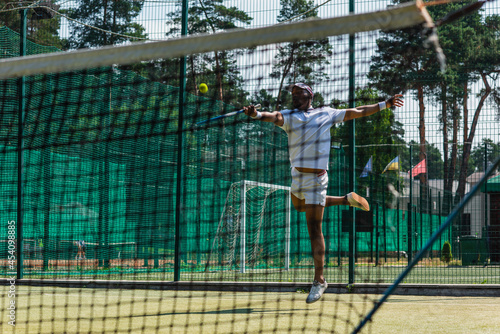 African american sportsman jumping while playing tennis near net