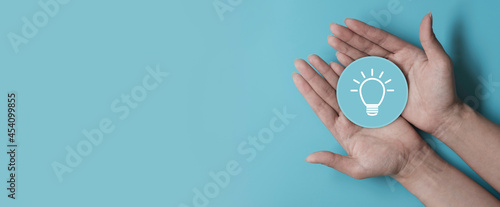 Fototapeta Naklejka Na Ścianę i Meble -  Idea innovation and inspiration concept, Woman hand holding light bulb icon on blue paper cut, concept creativity with bulbs that shine glitter, Inspiration ideas for sustainable business development