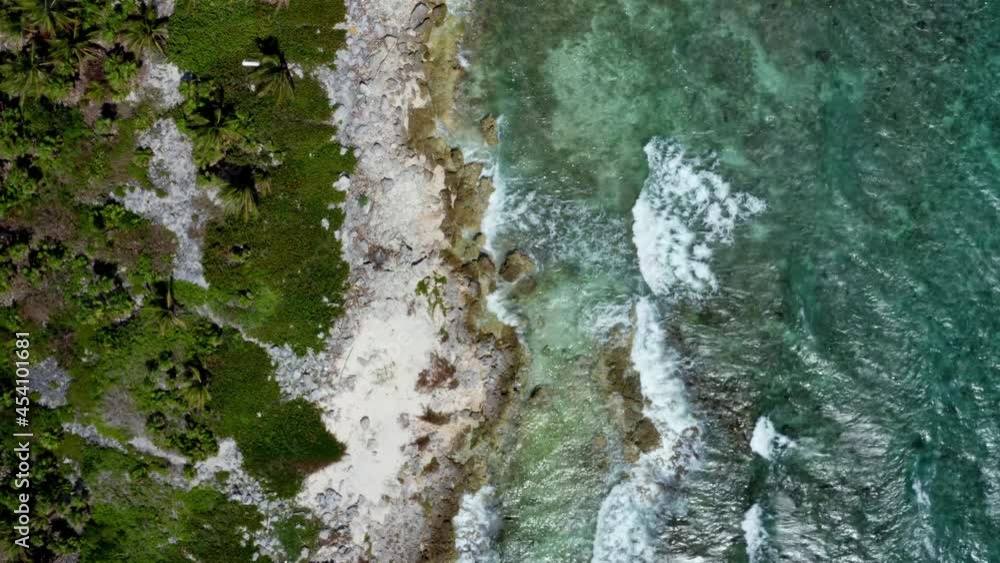 Beautiful aerial bird's eye drone top view of a tropical barren beach with clear turquoise water, white sand, palm trees, and waves crashing into rocks near Riviera Maya, Mexico near Cancun. Beautiful aerial bird's eye drone top view of a tropical barren beach with clear turquoise water, white sand, palm trees, and waves crashing into rocks near Riviera Maya, Mexico near Cancun.