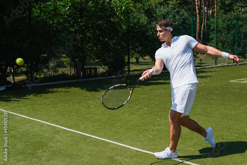 Side view of athletic sportsman holding racket near blurred ball on court