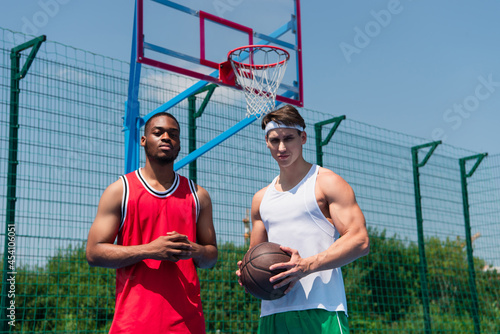 Multiethnic basketball players holding ball on playground