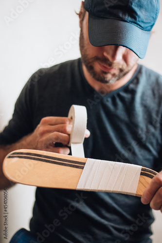 Canvas Print Bearded male ice hockey player wraps tape around hook hockey sticks to protect a