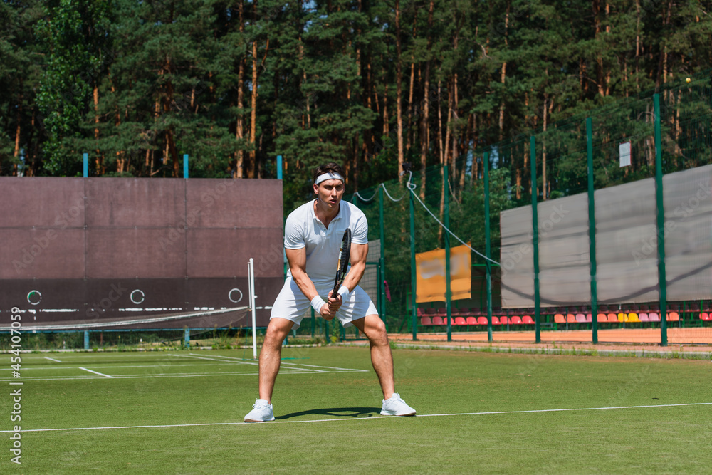 Sportsman in white sportswear holding tennis racket on court