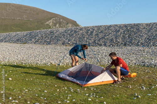 Camping people outdoor lifestyle couple putting up a tent in nature rocky beach. © Simon