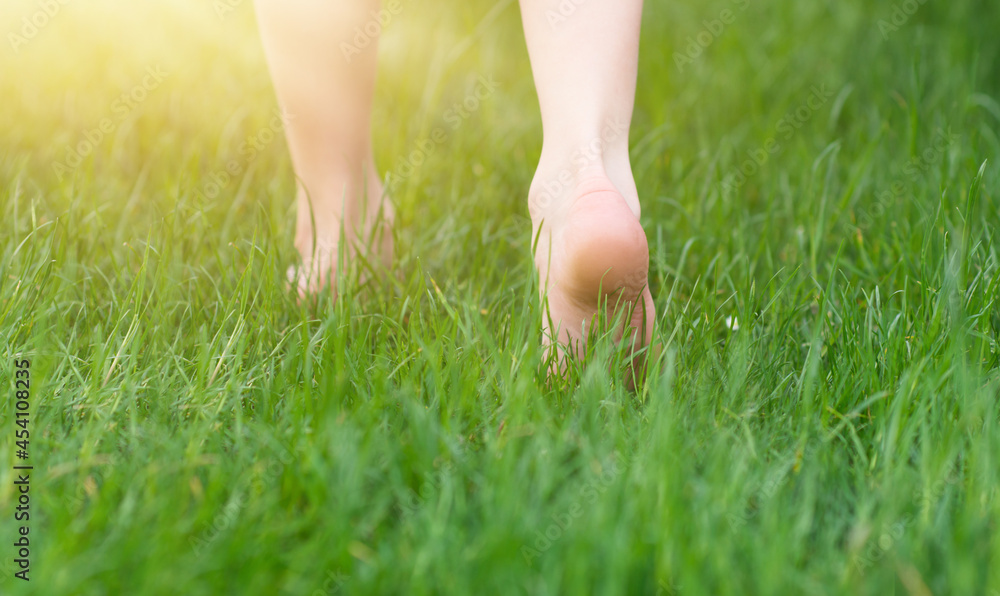 Kid foot walking in green grass on garden. Barefoot concept and healthy feet.