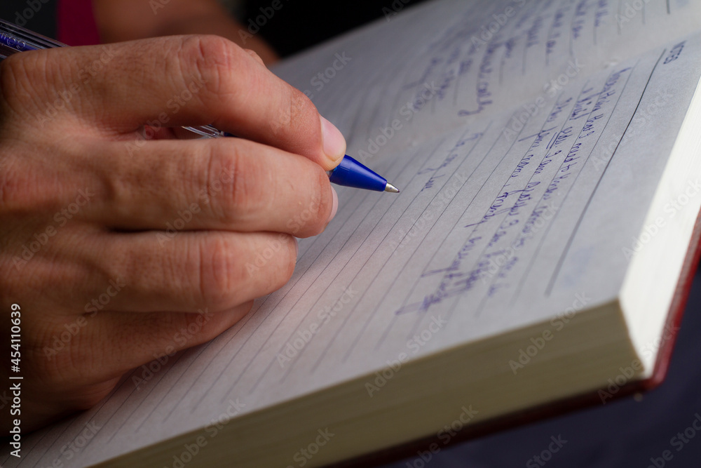 A man is writing with a blue pen on a notebook.selective focus A man is writing with a blue pen on a notebook.selective focus
