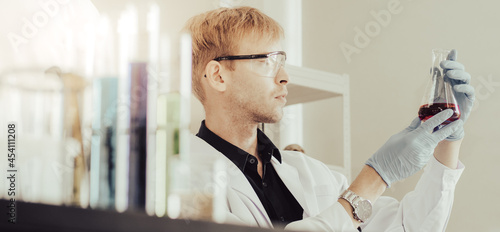 Male chemist looking at sample chemical liquid in beaker study for medicine development. Scientist wears protective gloves experiments and research innovative medicine in a scientific laboratory. 