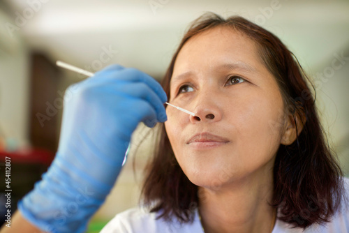 A doctor with gloves taking a nasal swab from an Asian person to test for possible coronavirus infection. Nasal mucus testing for viral infections. Woman getting tested for Covid19.
