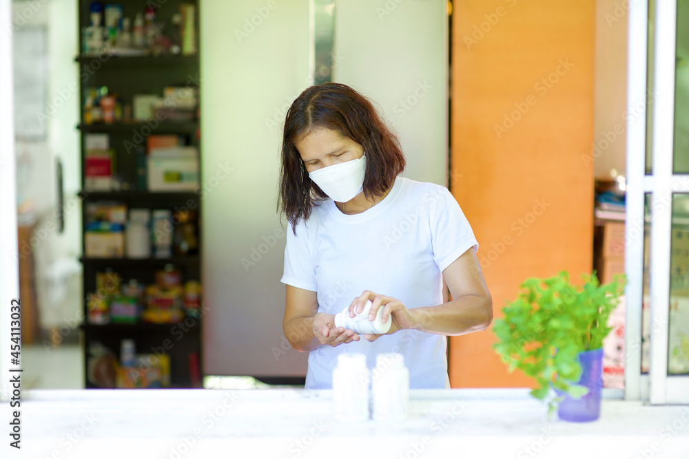 Asian woman self quarantine at home taking medication.Lady having medicine or supplement for illness while wearing mask.Adult boosting immune system with vitamin C.